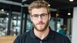 © PaulShlykov - Confident young man with glasses and a beard smiling in a modern indoor setting