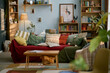 © Seventyfour - Interior of cozy living room with mix of colorful cushions, wooden bookshelves, indoor plants, cozy lighting, and eclectic decor
