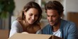 © Iryna - Young caucasian couple smiling while unboxing a cardboard box in new home