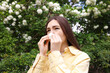 © New Africa - Woman with paper tissue suffering from seasonal pollen allergy near blossoming shrub on spring day