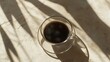 © keshia - A cup of black coffee on a table with sunlight casting shadows