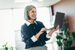 © deagreez - Confident mature businesswoman working on laptop in contemporary office environment with natural lighting indoors.