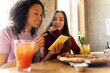© Maria Vitkovska - Two friends enjoying pizza and drinks while looking at smartphone in pizzeria