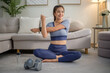 © wattana - Fit Asian woman in sportswear preparing her muscles with a full-body warm-up cozy living room.