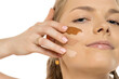 © vladimirfloyd - Close-up of young woman with contemplative expression displaying three different foundation shades swatched on cheek, comparing makeup colors against white background