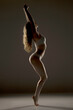 © vladimirfloyd - Dramatic silhouette of woman in white underwear stretching upward on tiptoes with raised arms, showcasing elegant body contours against dark background