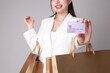 © Auttapol - Confident businesswoman showcasing credit card while holding shopping bags on gray background in modern retail environment