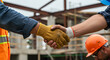 © SULTAN - Construction workers shaking hands on a construction site with safety gear and building framework visible