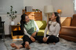 © Crystal - Two happy female friends spending leisure time together at home, enjoying conversation and laughter in a cozy living room setting