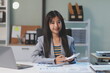 © Phanphen - Portrait of young Asian businesswoman in suit, woman smiling and work at workplace inside office, accountant with calculator behind paper phone signing contracts and financial reports