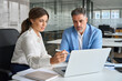 © insta_photos - Two professional business executives team people working together on computer in office. Female lawyer or bank manager consulting mature client about financial project using laptop talking at meeting.