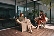 © insta_photos - Two happy diverse business women talking in cozy office sitting in chairs. Smiling professional ladies partners drinking coffee having conversation taking notes at work break in creative green space.