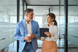 © insta_photos - Two busy business people executive team talking walking in office. Mature professional business man and woman partners working together having conversation in office using digital tab. Authentic photo