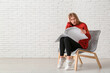 © Pixel-Shot - Emotional young woman reading newspaper while sitting on chair near white brick wall