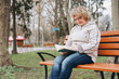© anatoliycherkas - Senior woman enjoying reading a book on a park bench