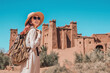 © EdNurg - Tourist with backpack and hat enjoying view of fortified city of Ait Benhaddou, a world heritage site in Morocco