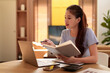 © snowing12 - Asian woman working from home using laptop and reading a book Adult student learning online education concept and search information online using computer at home