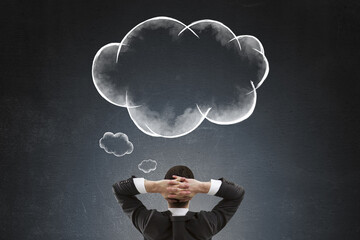Fototapete - Rear view of businessman thinking with hands behind head looking at cloud-shaped thought bubbles on dark background symbolizing brainstorming.