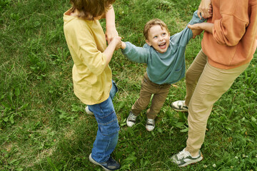 Wall Mural - Top view of young boy laughing while holding hands with mother and brother playing joyfully in green grass