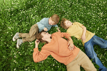Wall Mural - Top view of mother with two boys lying on green grass in clover field together enjoying nature, copy space