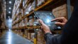 © Banstanks - Warehouse worker using a tablet to manage inventory among stacked boxes in a busy distribution center