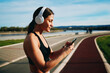 © djile - Young sportswoman wearing headphones is choosing music on smartphone before running in city park