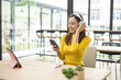 © Kield KD - A woman is sitting at a table with a pink tablet and a cell phone. She is wearing headphones and she is listening to music. The scene suggests a relaxed and leisurely atmosphere