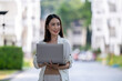 © Wasana - A woman is holding a laptop in a city street
