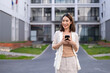© Wasana - A woman is standing in front of a building with a cell phone in her hand