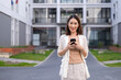 © Wasana - A woman is standing in front of a building with a cell phone in her hand