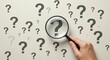 © ibrahim - Hand Holding Magnifying Glass to Search for Answers Among Scattered Question Marks