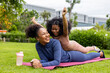 © Akarawut - African American mother and young daughter are lying down and playing ride after having yoga exercise public park for weekend leisure and happiness