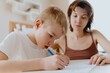 © looking2thesky - A loving mother and her son work together on homework at the kitchen table, symbolizing family support, education, and care. The scene highlights the importance of parental guidance