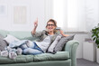 © amedeoemaja - Woman lying on couch with smart glasses and credit card, using virtual screen
