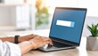 © M - Person typing on a laptop keyboard with a search bar displayed on the screen, surrounded by a bright workspace and greenery