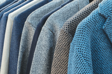 Poster - A row of blue and gray sweaters are hanging on a rack. The blue sweater is the most prominent