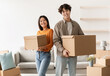 © Prostock-studio - Portrait of young Asian woman and her cool boyfriend holding cardboard boxes, looking at camera and smiling in new home. Millennial spouses moving and settling into rented apartment