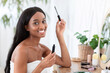 © Prostock-studio - Morning routine makeup. Pretty millennial african american woman applying mascara on eyelashes and looks at camera, sits at table with cosmetics, in modern bedroom interior in morning, copy space