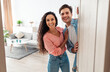 © Prostock-studio - Portrait of cheerful couple inviting visitor people to enter their home, happy young guy and lady standing in doorway of modern apartment, millennial family holding door looking out together