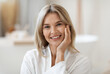 © Prostock-studio - Portrait of smiling beautiful middle aged woman touching her cheek, demonstrating her smooth face skin after using anti-aging cosmetics in the morning, bathroom interior, closeup, copy space