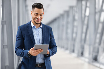 Happy Arab Businessman Booking Hotel Online While Using Digital Tablet In Airport, Handsome Middle Eastern Entrepreneur With Tab Computer Standing In Terminal, Waiting For Flight Boarding, Copy Space