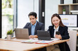 © David - Young Asian Man and Woman manager project on laptop in modern office. Two business people of professional working, studying, writing notes sit at desk
