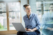 © Westend61 - Businesswoman with laptop sitting by window in office