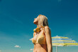 © Westend61 - Woman in a swimsuit with headphones enjoying a sunny day outdoors under a blue sky.