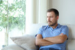 © Antonioguillem - Pensive sad man looking through a window on a couch