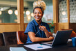 © (JLco) Julia Amaral - Smiling young woman sitting at a desk with a laptop and papers
