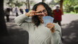 © Krakenimages.com - Middle-aged woman in a city street holds malaysian ringgit while making a peace sign with blurred park background and pedestrians.
