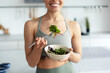 © Maria Vitkovska - Smiling sportswoman eating healthy salad in the kitchen, selective focus on hands