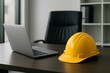 © CandyLove - A laptop and a yellow hard hat sitting on a desk in an office with a chair and shelves behind it