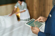 © pressmaster - Hotel staff member holding tablet while another prepares room, focusing on efficiency and coordination in hospitality service